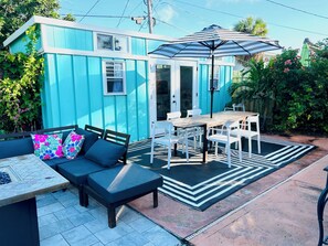 A blue house with a patio area featuring a table and chairs, a sofa with cushions, and a striped umbrella.