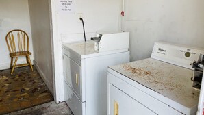 A laundry room with two white Whirlpool washers, a wooden chair, and a sign indicating laundry time from 08:00 AM to 10:00 PM. - Royal Palms Motel & RV Park (New Orleans)