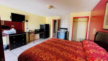 A hotel room with a bed, a desk, a refrigerator, and a stove.