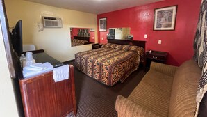 A hotel room with a bed, a sofa, a desk, and a television. - Royal Palms Motel & RV Park (New Orleans)