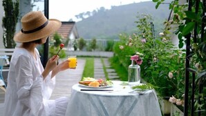 Eine Person sitzt an einem Tisch im Freien und genießt eine Mahlzeit, ein Getränk und eine Blumenvase.