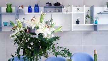 A room with a blue chair, a vase with white flowers, and shelves with various items.
