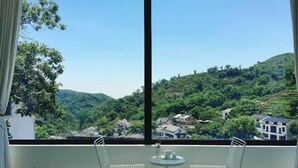 Ein Balkon mit zwei Stühlen und einem kleinen Tisch, mit Blick auf eine hügelige Landschaft mit Häusern.