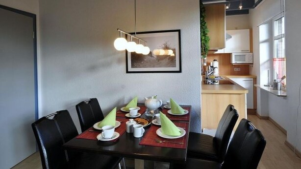 Een eetgedeelte met een tafel gedekt voor vier personen, een moderne hanglamp en een ingelijst kunstwerk aan de muur.