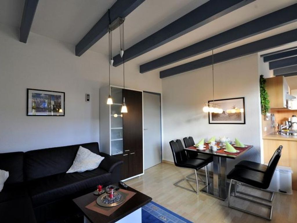 A modern living room with a black sofa, dining table with chairs, and pendant lights.