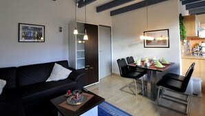 Een moderne woonkamer met een zwarte bank, een eettafel met stoelen en hanglampen.