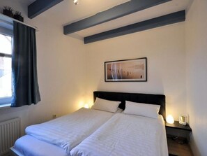 A double bed with white linens, a framed picture on the wall, and a bedside table with a lamp. - Vacation apartment Huus vörd Diek Nelkenweg 4 Apartment 1 - Huus vör`d Diek (Neuharlingersiel)