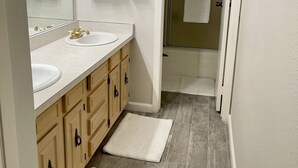 A bathroom with a double sink, wooden cabinets, a mirror, and a shower area. - Two bedroom right off the strip (Las Vegas)
