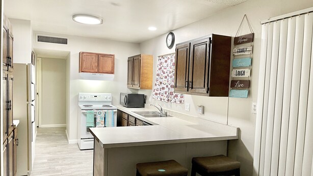 A compact kitchen with a central island, wooden cabinets, a microwave, and a clock on the wall. - Two bedroom right off the strip (Las Vegas)