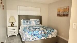 A bedroom with a bed, a nightstand, a lamp, and a painting on the wall. - Two bedroom right off the strip (Las Vegas)
