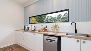 Una cocina moderna con armarios blancos, encimera de madera, lavavajillas y ventana con vistas a árboles.