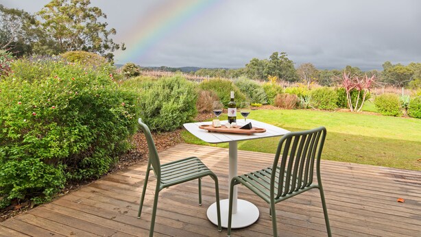 Una terraza con una mesa para dos, rodeada de abundante vegetación y una vista distante de árboles.
