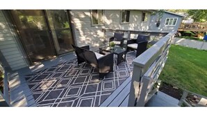 A covered patio with outdoor furniture, a patterned floor, and a view of a house with a deck. - All you need for your home away from home in MN (Sauk Rapids)