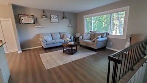 A spacious living room with a large window, a sofa, a coffee table, and a staircase with a railing. - All you need for your home away from home in MN (Sauk Rapids)