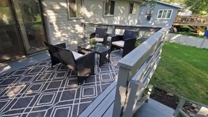 A covered patio with outdoor furniture, a patterned floor, and a view of a house with a deck. - All you need for your home away from home in MN (Sauk Rapids)