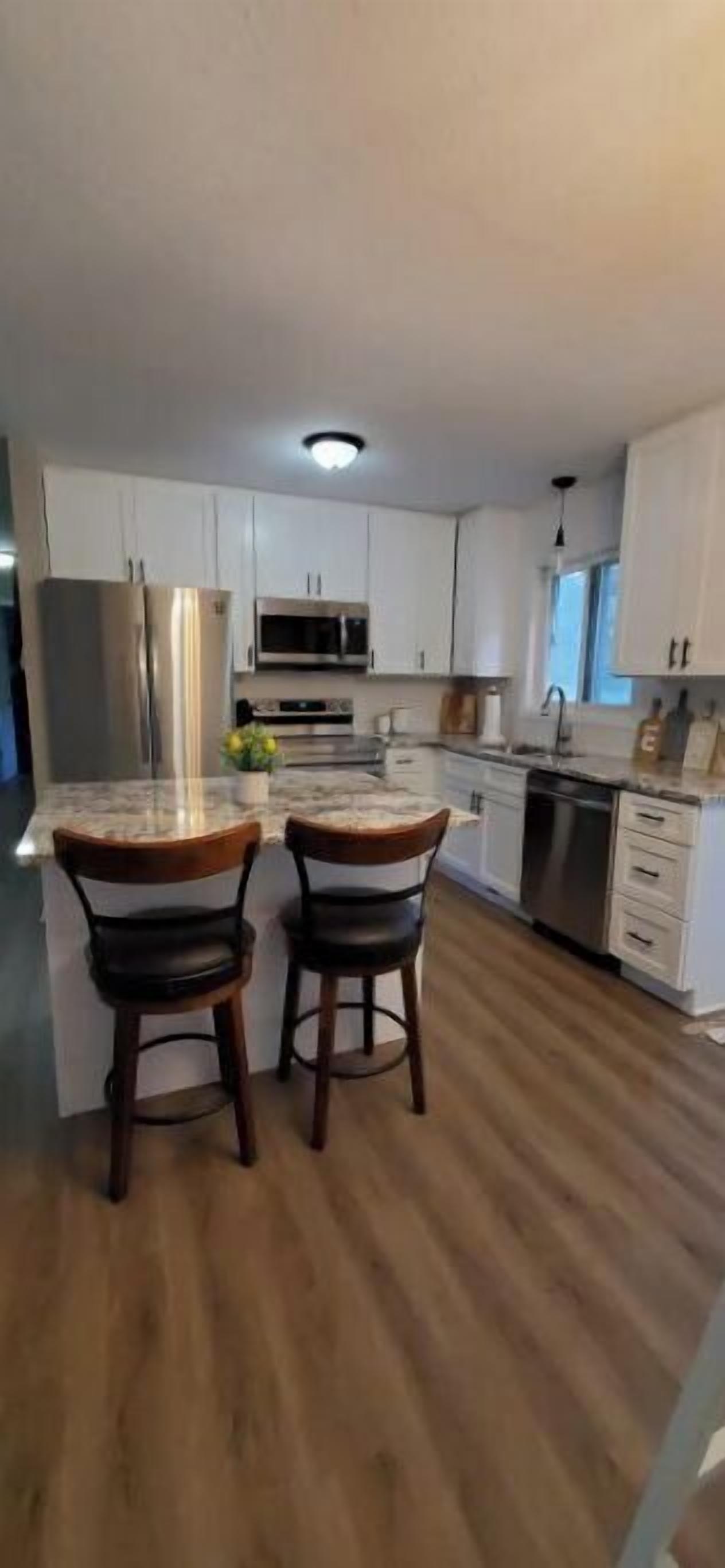 A modern kitchen with white cabinets, stainless steel appliances, and a wooden island with two chairs.