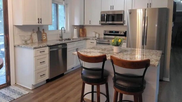 A modern kitchen with white cabinets, stainless steel appliances, and a marble countertop. - All you need for your home away from home in MN (Sauk Rapids)