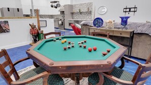 A pool table with balls, surrounded by chairs, in a room with a tiled floor and white walls.