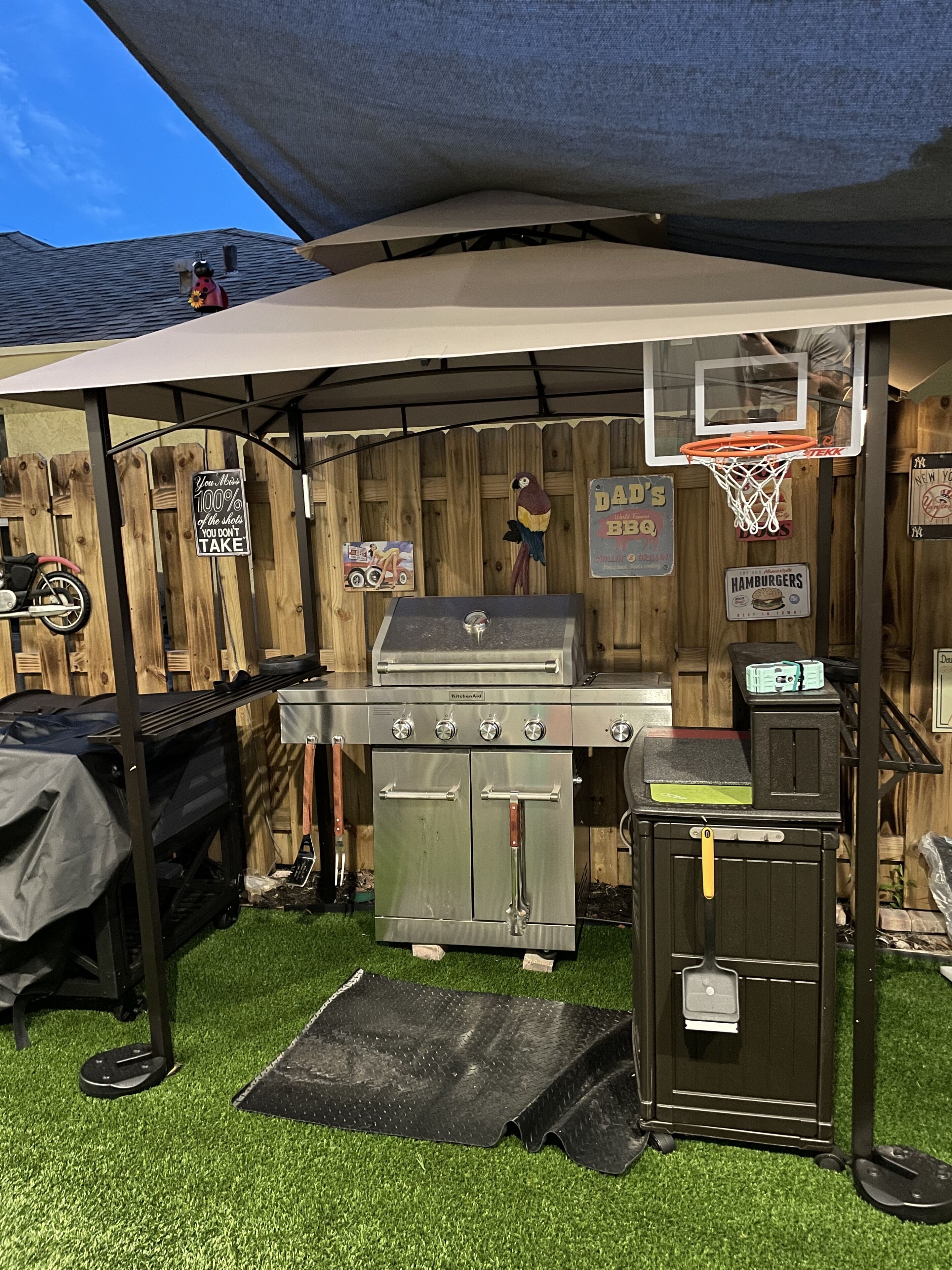 Een achtertuin met een barbecue, een basketbalring en een houten omheining.