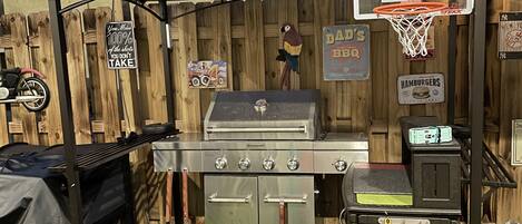 Een achtertuin met een barbecue, een basketbalring en een houten omheining.