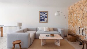 Un saló modern amb un sofà seccional gris, una taula baixa de marbre, una obra d'art abstracta emmarcada, una paret decorativa de pedra i una làmpada de peu.