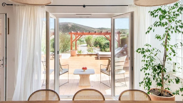 Zona de menjador amb taula i cadires, una pérgola i vista a un jardí i muntanyes.