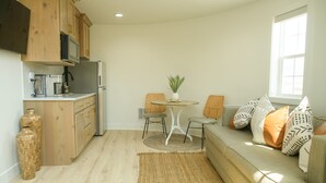 Um espaço de estar compacto com cozinha compacta, área de refeições com mesa e cadeiras, e um sofá com almofadas.