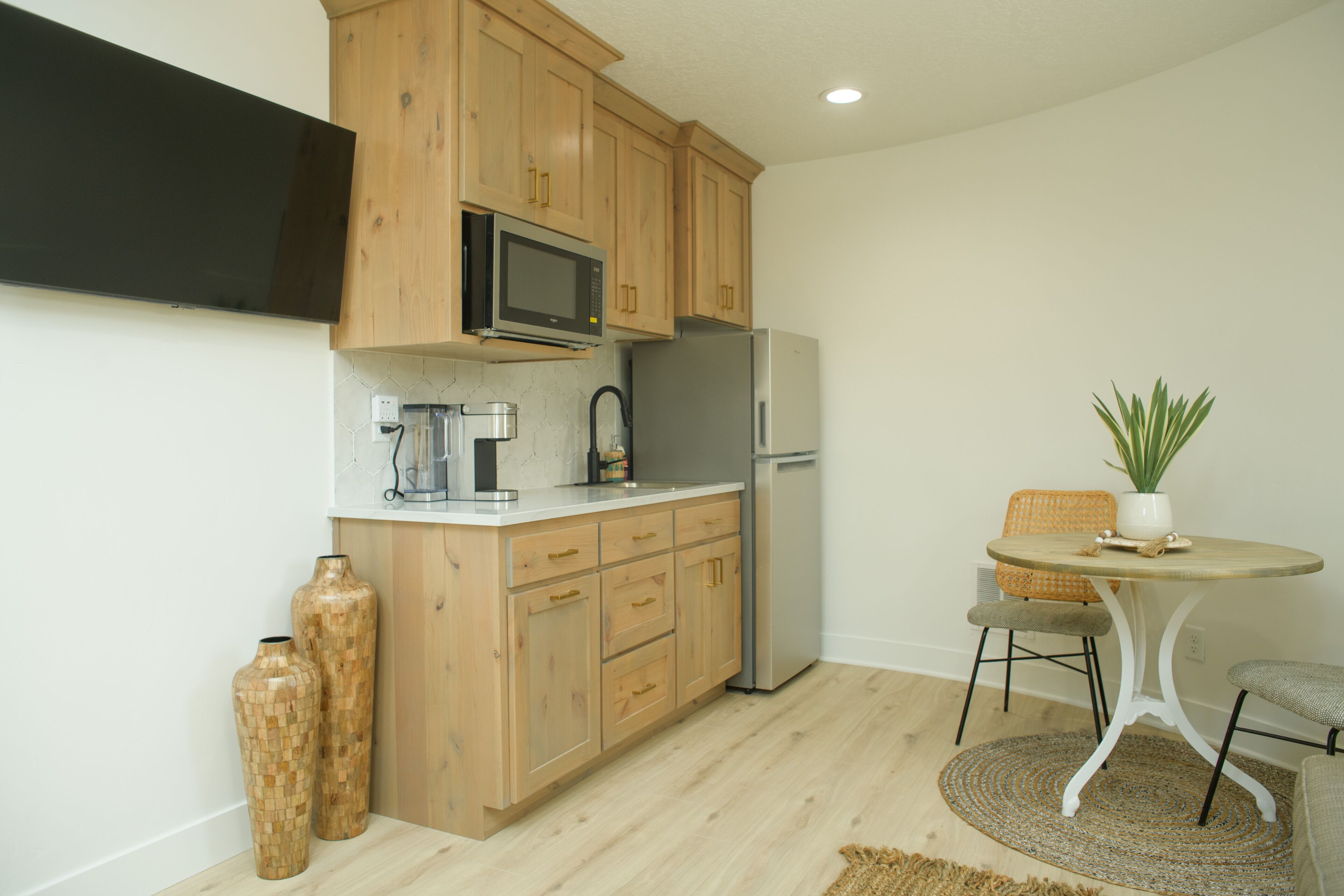 A compact kitchen with wooden cabinets, a microwave, a refrigerator, a coffee maker, and a small dining table with chairs.