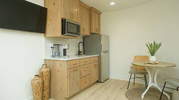 A compact kitchen with wooden cabinets, a microwave, a refrigerator, a coffee maker, and a small dining table with chairs.
