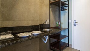Un baño moderno con encimera de granito, lavamanos y espejo. Hay dos vasos pequeños sobre la encimera y un perchero encima del lavamanos.