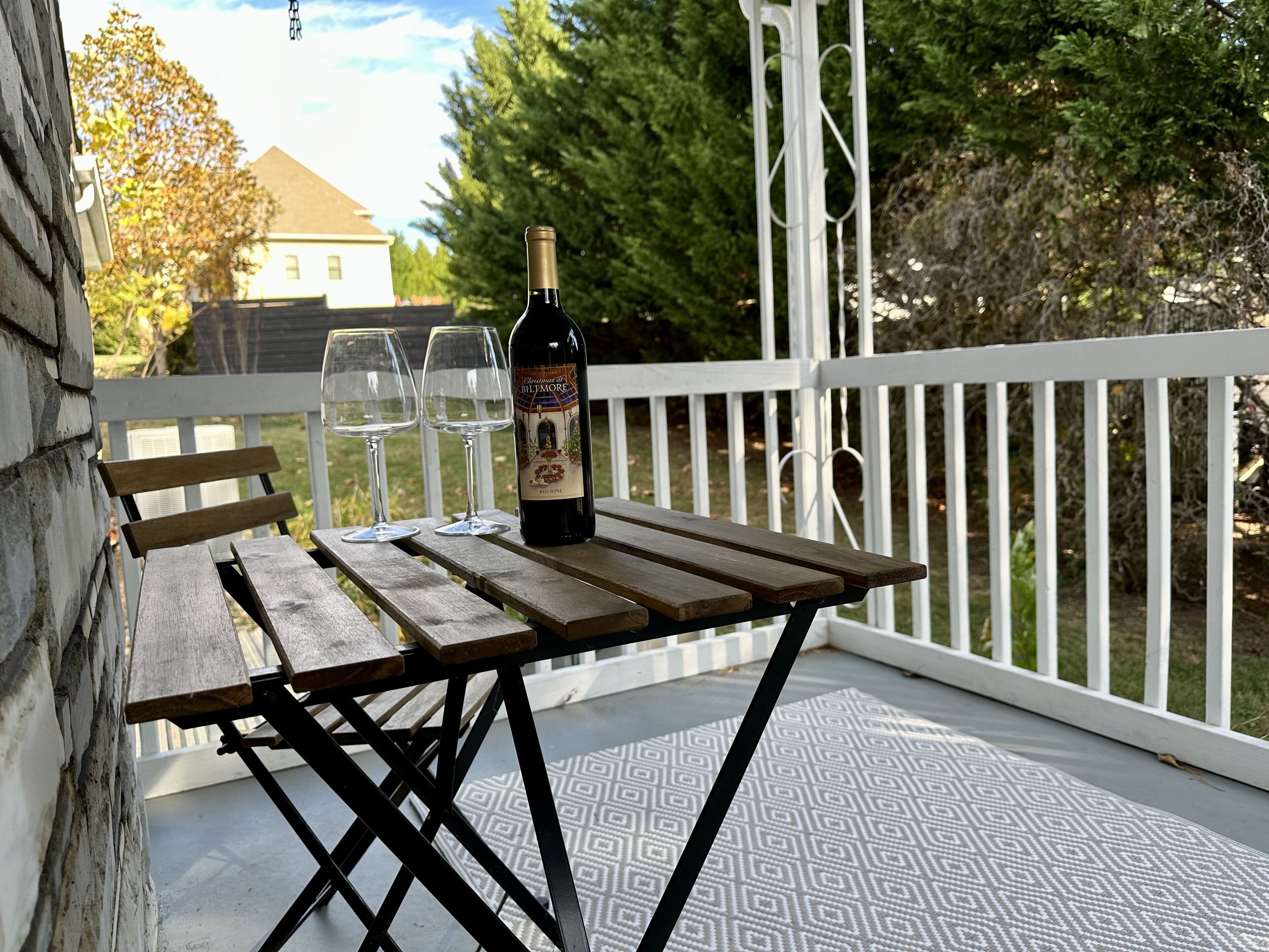 Una mesa de madera con una botella de vino tinto y dos copas en un porche.