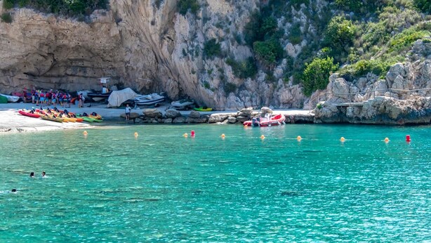 Zona costera con agua turquesa cristalina, kayaks y un bote inflable rojo.