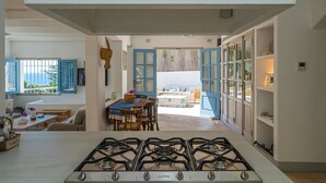A modern kitchen with a gas stove, open blue doors leading to a dining area with a view of the sea. - Son de Mar - By Almarina Villas (JÁVEA)