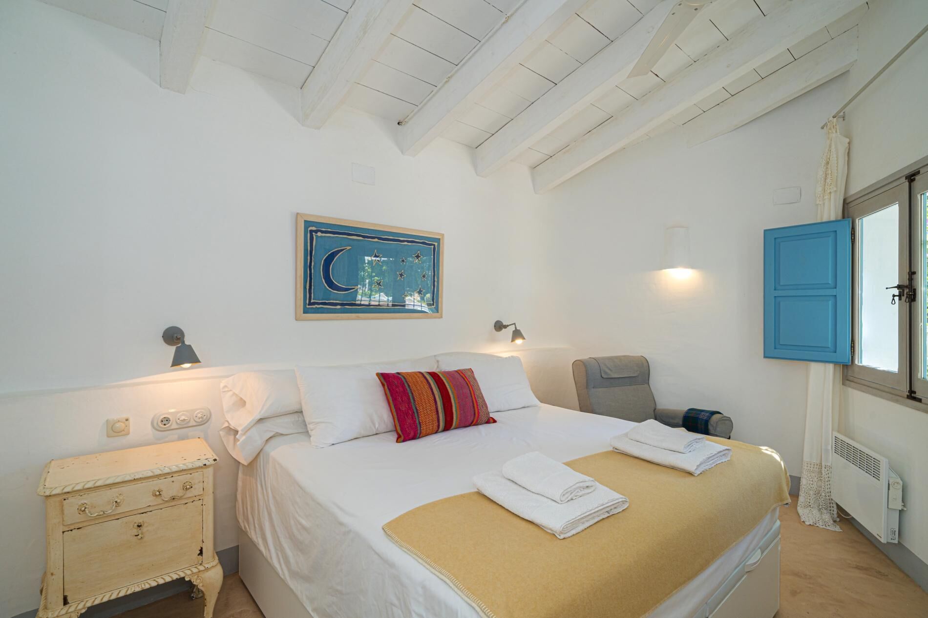 A bedroom with a bed, a nightstand, a dresser, a painting, a lamp, a chair, and a window with blue shutters.