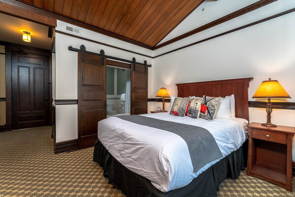A hotel room with a large bed, wooden headboard, two bedside lamps, and a sliding door closet. - The Landing 207 Deluxe Queen Suite, Jetted Tub (Chelan)