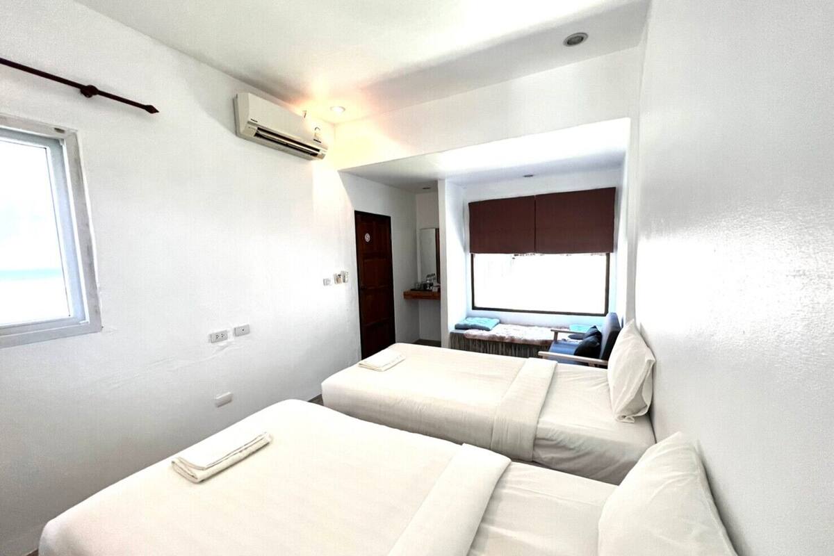 A small, compact room with two single beds, a window, and a built-in desk with a chair.