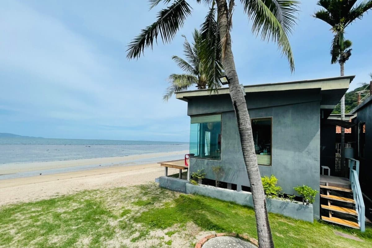A modern beach house with a large glass window, a concrete deck, and a view of the ocean.