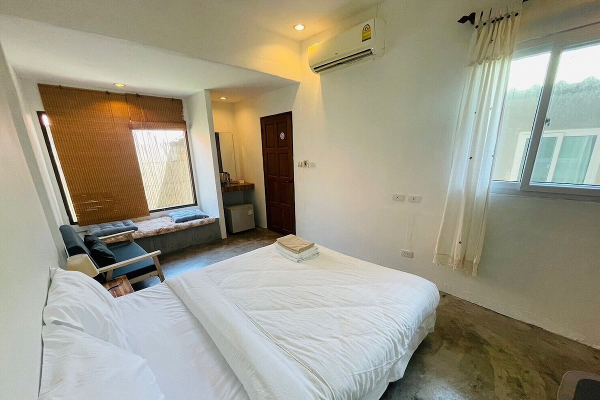 A bedroom with two beds, a window with curtains, a built-in bench, and an air conditioning unit.