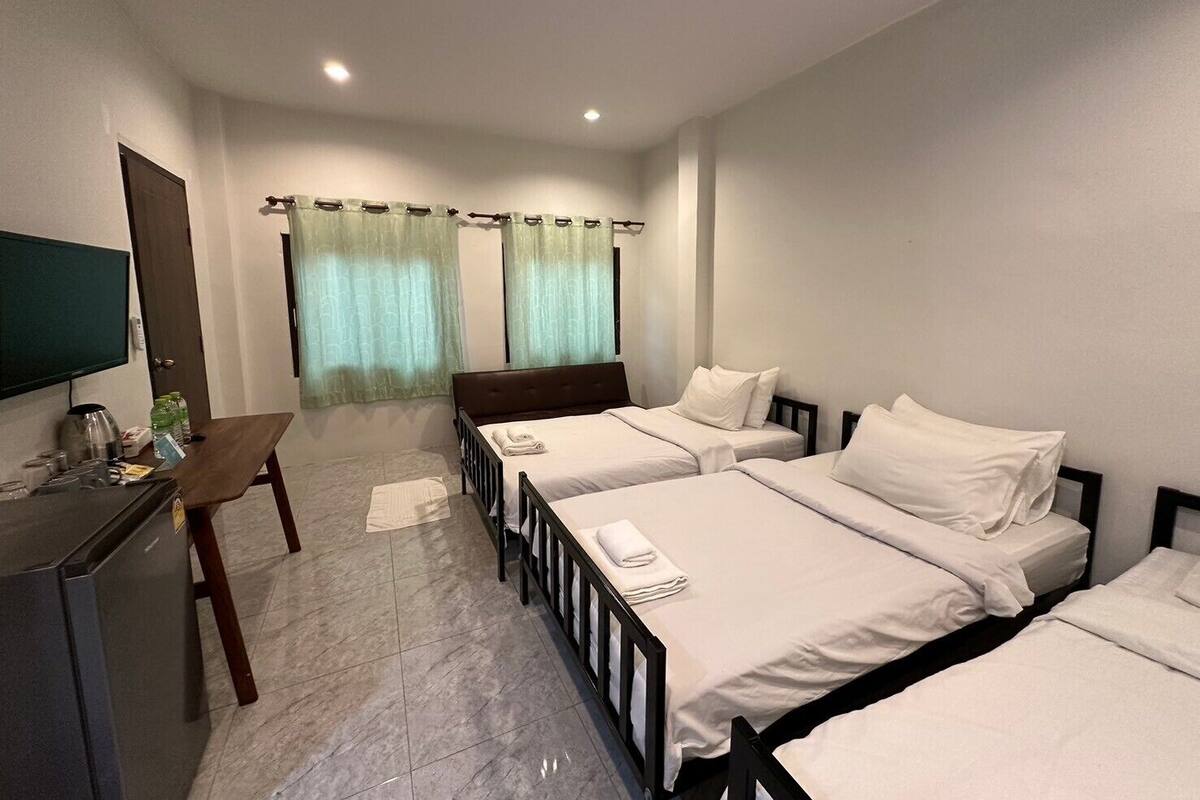 A hotel room with three single beds, a desk with a chair, a television, and a window with curtains.