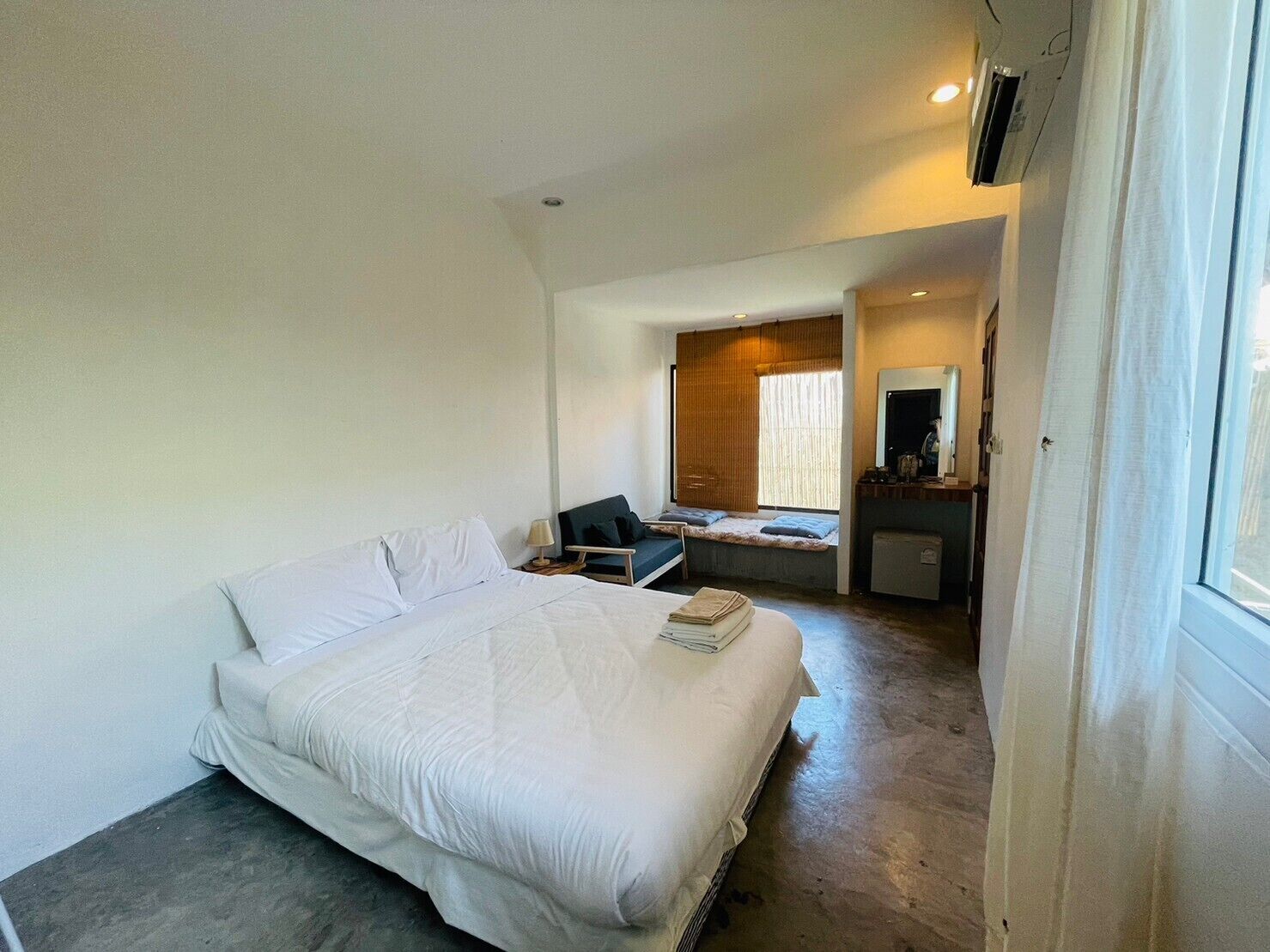 Une chambre à coucher avec un lit, un bureau, une chaise, une petite table, un miroir et une fenêtre.