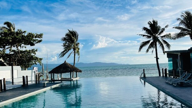 Piscina com vista para o mar, palmeiras e estrutura com telhado de palha.