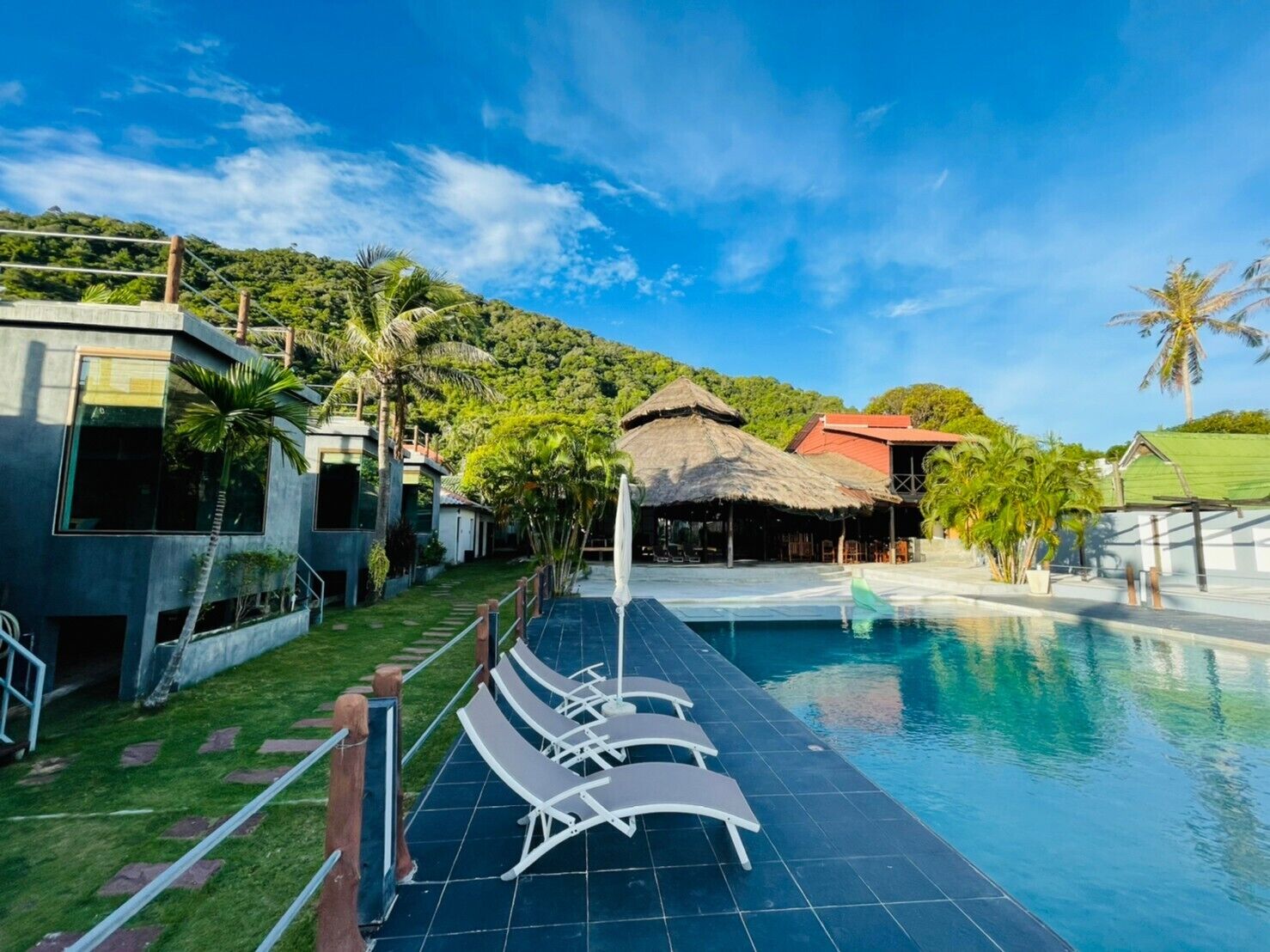 Ein Poolbereich mit Liegestühlen, einer Struktur mit Strohdach und Blick auf einen üppigen, grünen Hang.