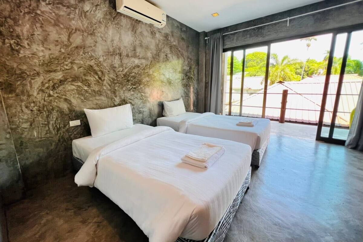 A modern hotel room with two beds, a large window, and a stone wall.