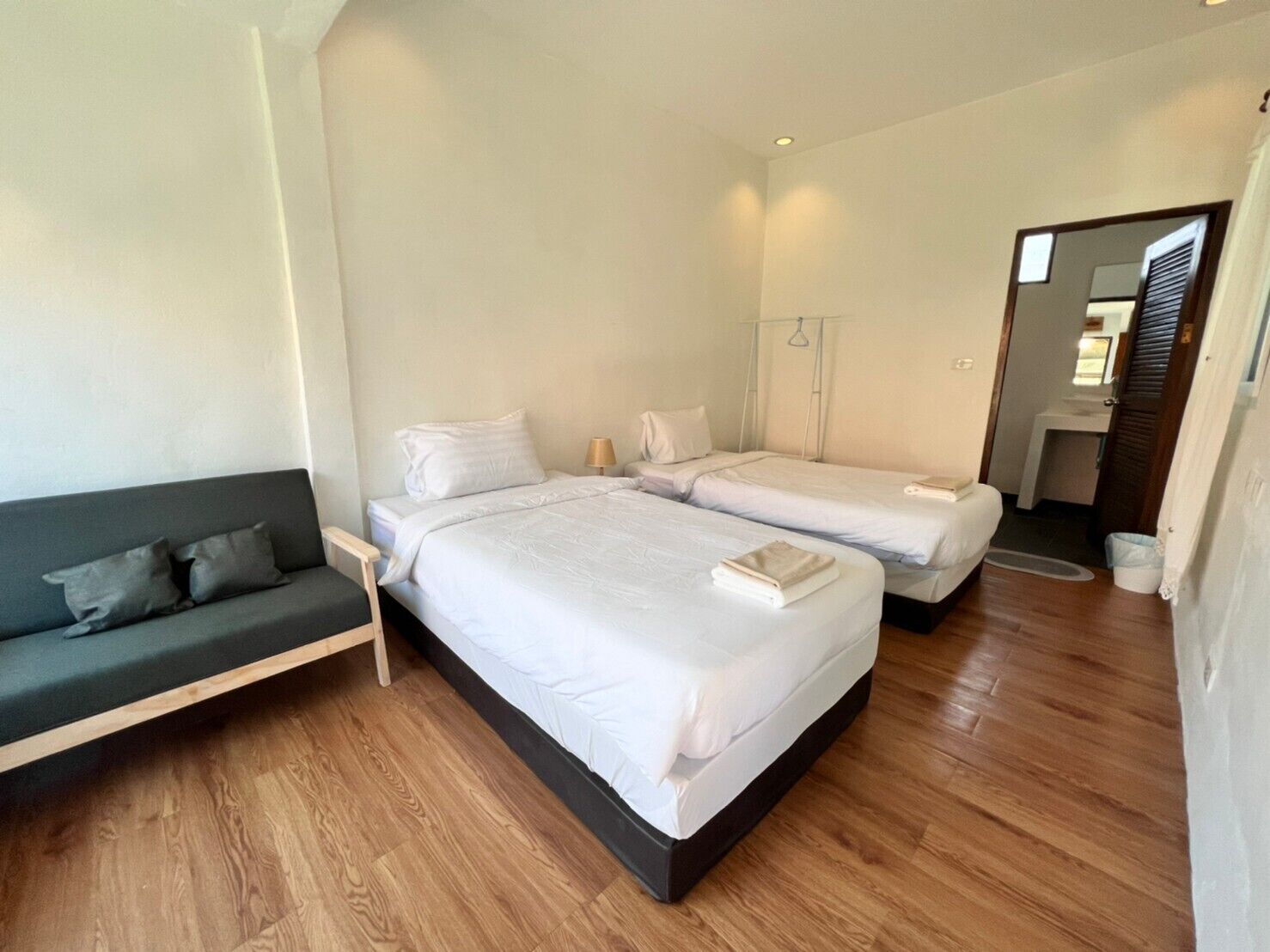 A modern hotel room with two single beds, a sofa, and a small bathroom.