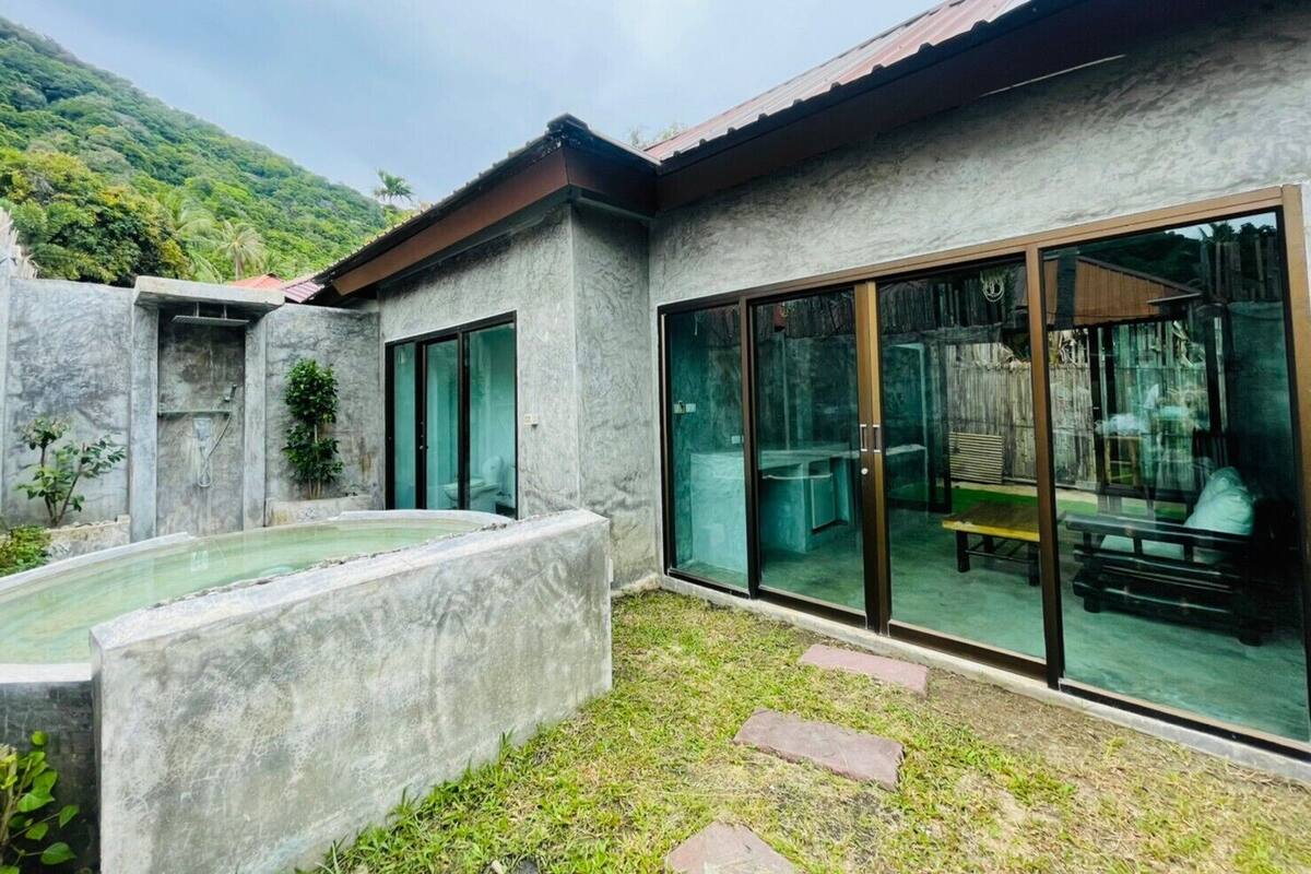 A modern house with a swimming pool, large glass doors, and a view of a lush green hill.