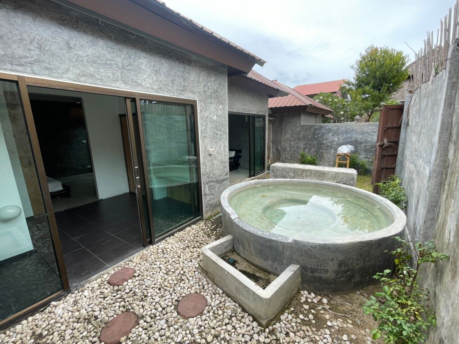A modern house with a glass door leading to a bedroom, a small outdoor hot tub, and a gravel patio.