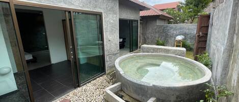 A modern house with a glass door leading to a bedroom, a small outdoor hot tub, and a gravel patio.