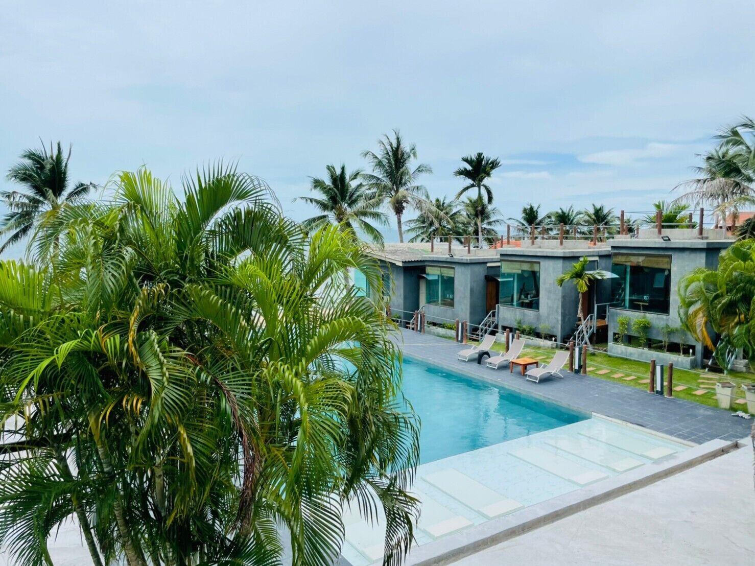 Un hôtel moderne doté d’une piscine, de palmiers et offrant une vue sur un ciel dégagé.