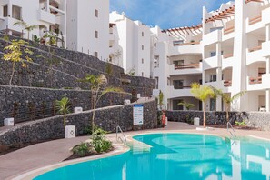 Um resort com piscina, edifícios brancos e um muro de pedra.