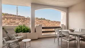 A modern outdoor patio with a dining area, including chairs and a table, overlooking a hilly landscape.